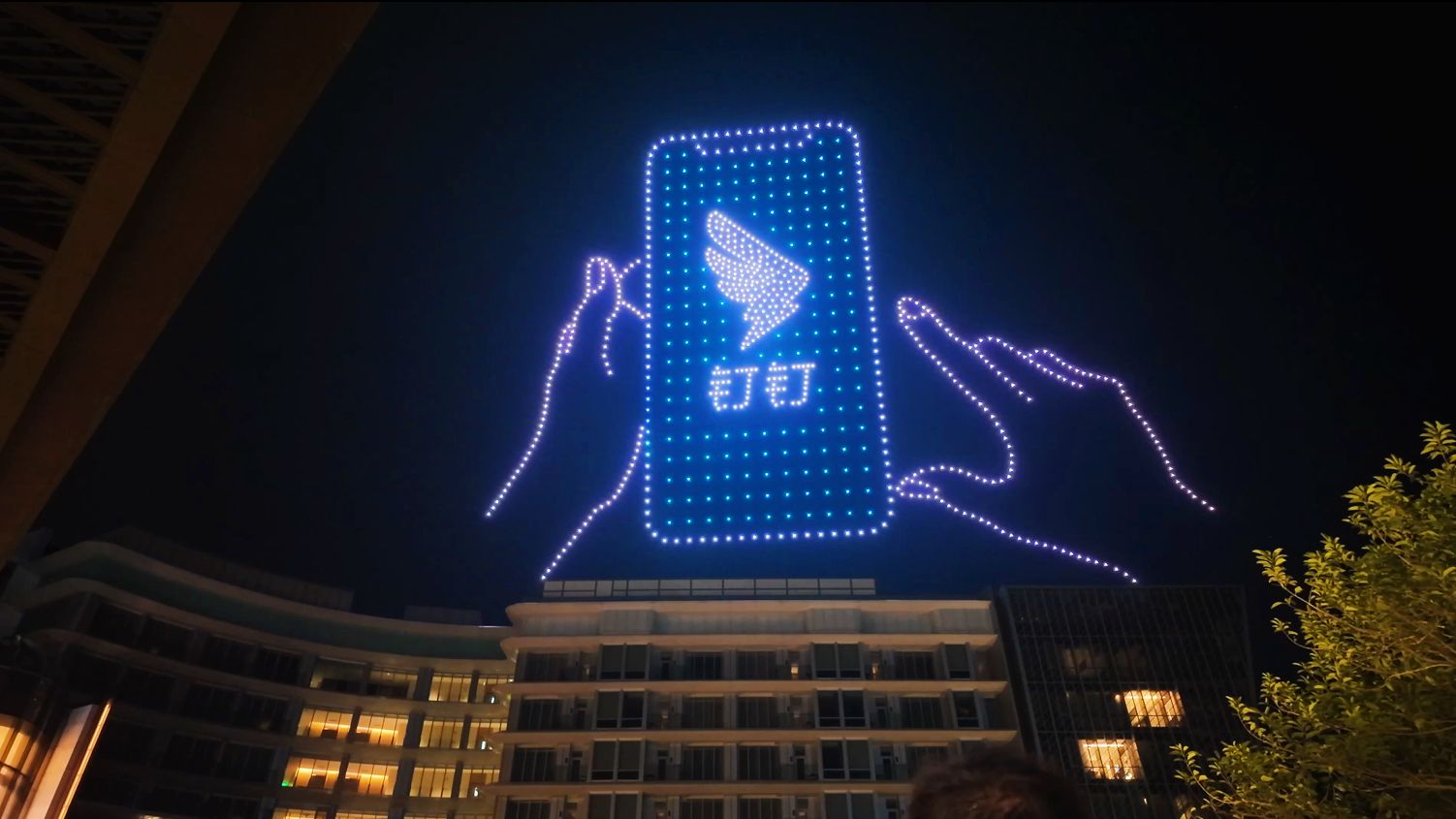 Drone light show forming a brand logo above a city